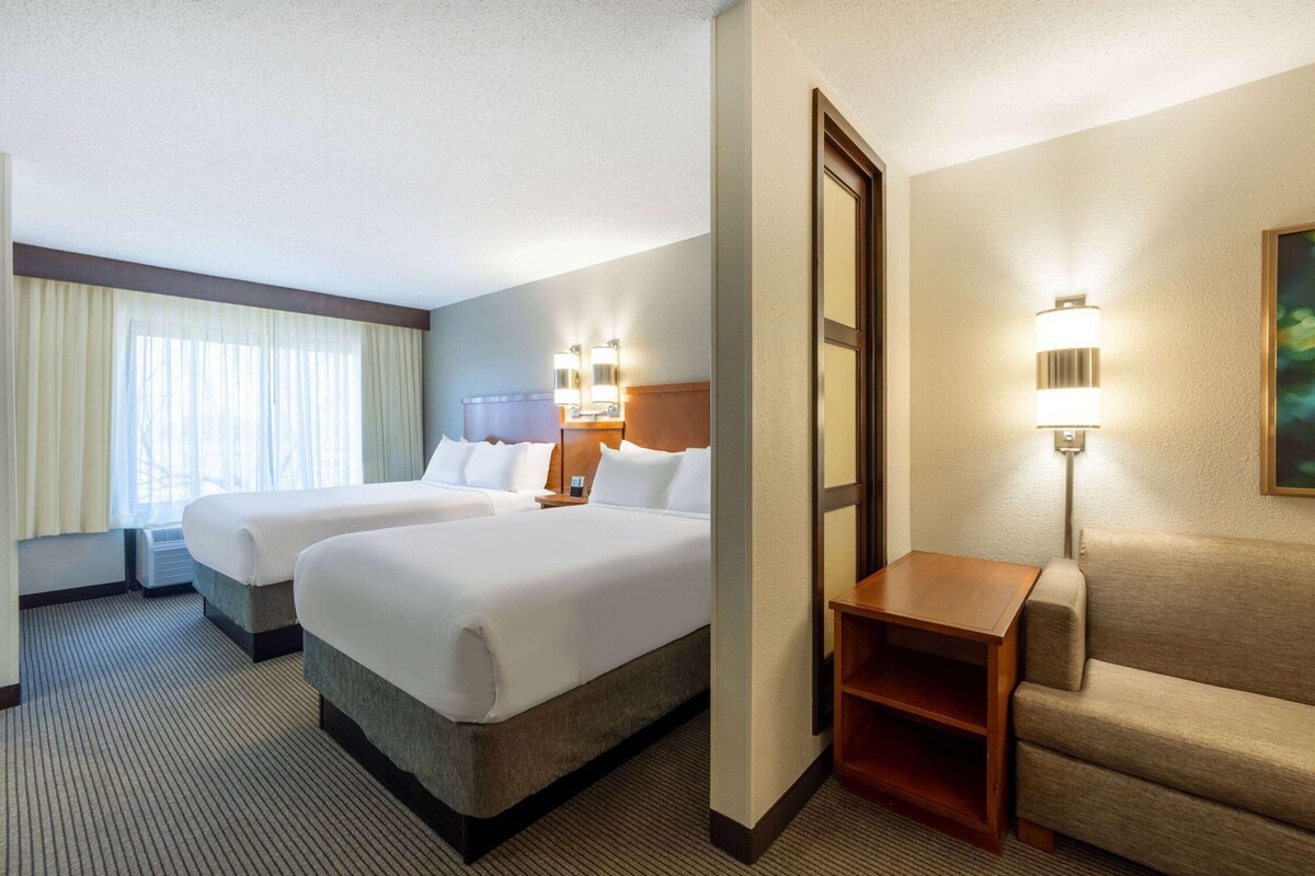 A hotel room with two beds, a sofa, a nightstand, and a lamp.