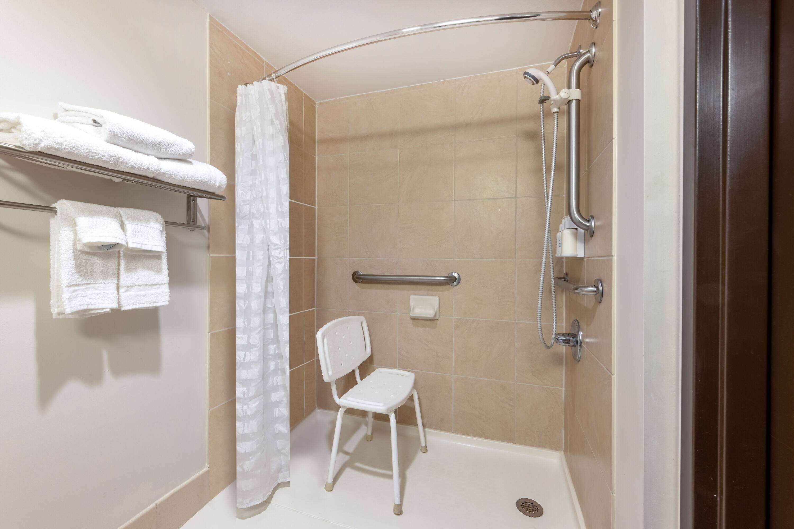 A shower area with a white chair, a towel rack with folded towels, and a shower control panel.