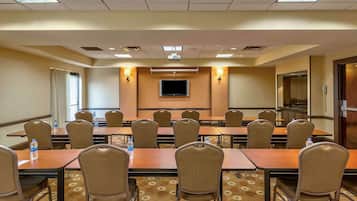 A conference room with a long table, chairs, a flat-screen TV, and a carpeted floor.