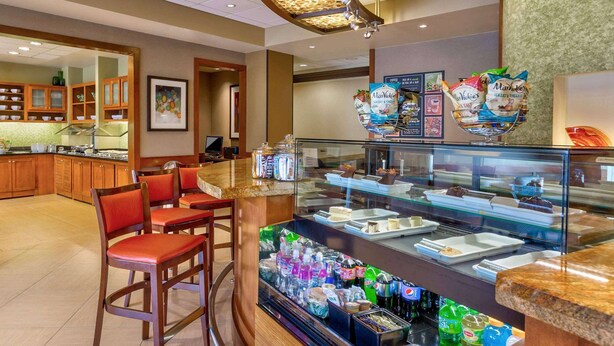 Zona de desayuno de hotel con mostrador, asientos y una vitrina con alimentos.