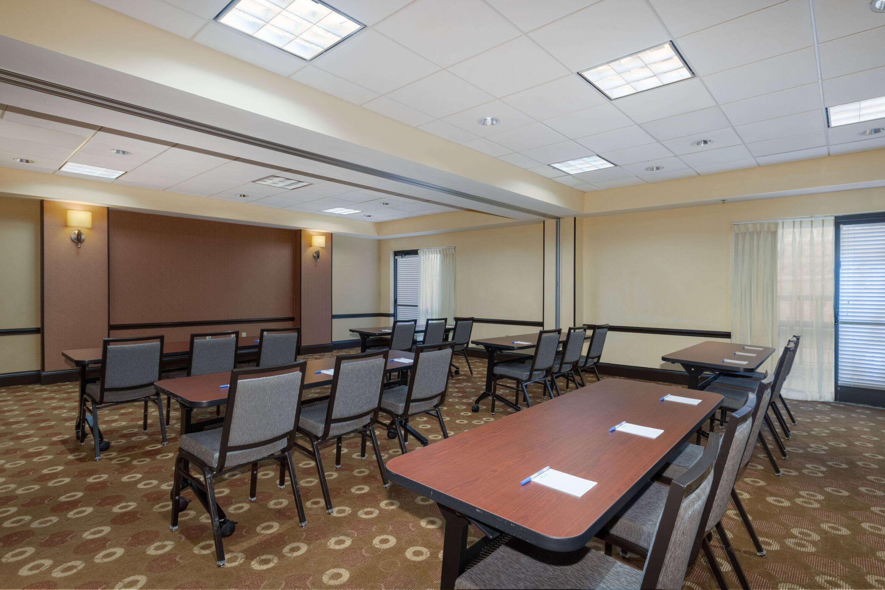 A conference room with multiple tables and chairs, carpeted floor, and ceiling lights.