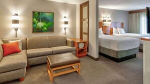 Habitación de hotel con sofá, una mesita, cama, mesita de noche, televisor montado en la pared y dos lámparas de pared.