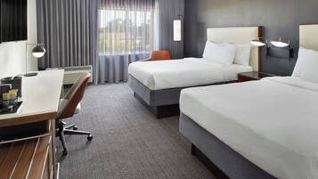 A hotel room with two beds, a desk, a chair, and a large window with curtains.