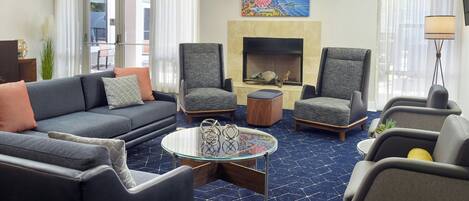 A modern living room with a sofa, two armchairs, a glass coffee table, and a fireplace.