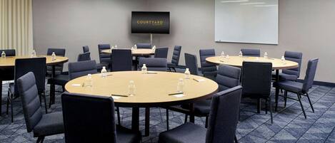 A conference room with multiple tables and chairs, a large screen, and a projector screen.