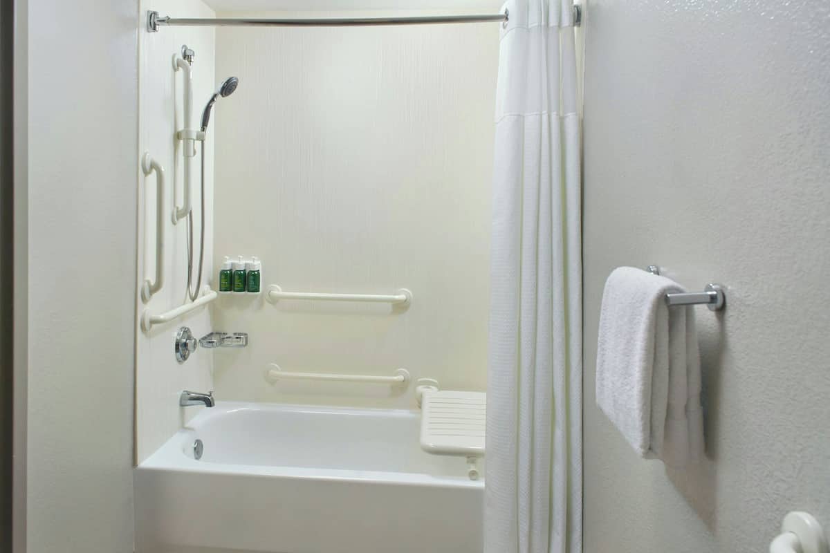 Un baño con bañera, ducha y barras de apoyo.