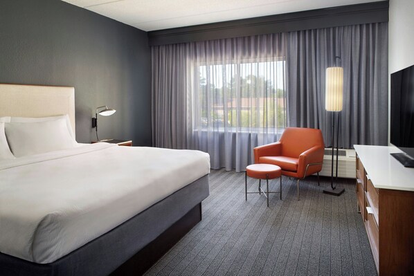 Una habitación de hotel con una cama grande, un escritorio, una silla naranja y un televisor.