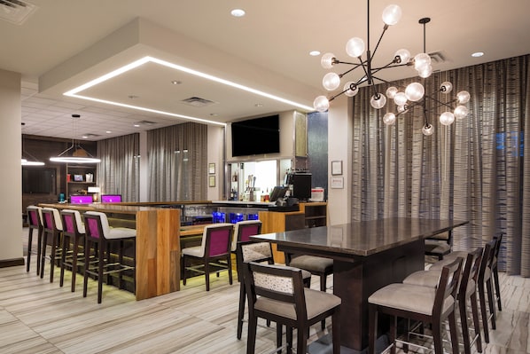 A modern bar area with a long counter, bar stools, and a unique chandelier. - Crowne Plaza Memphis Downtown by IHG (Memphis)