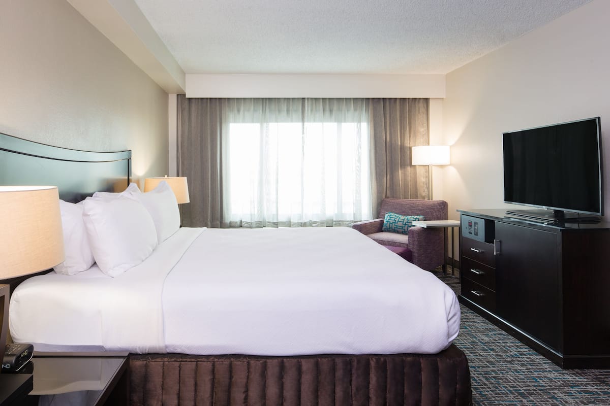 Habitación de hotel con una cama grande, un televisor, un escritorio con lámpara y una silla.