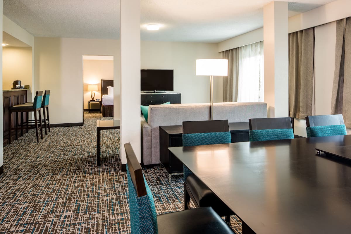 Una habitación de hotel con comedor, televisor, lámpara y cama.