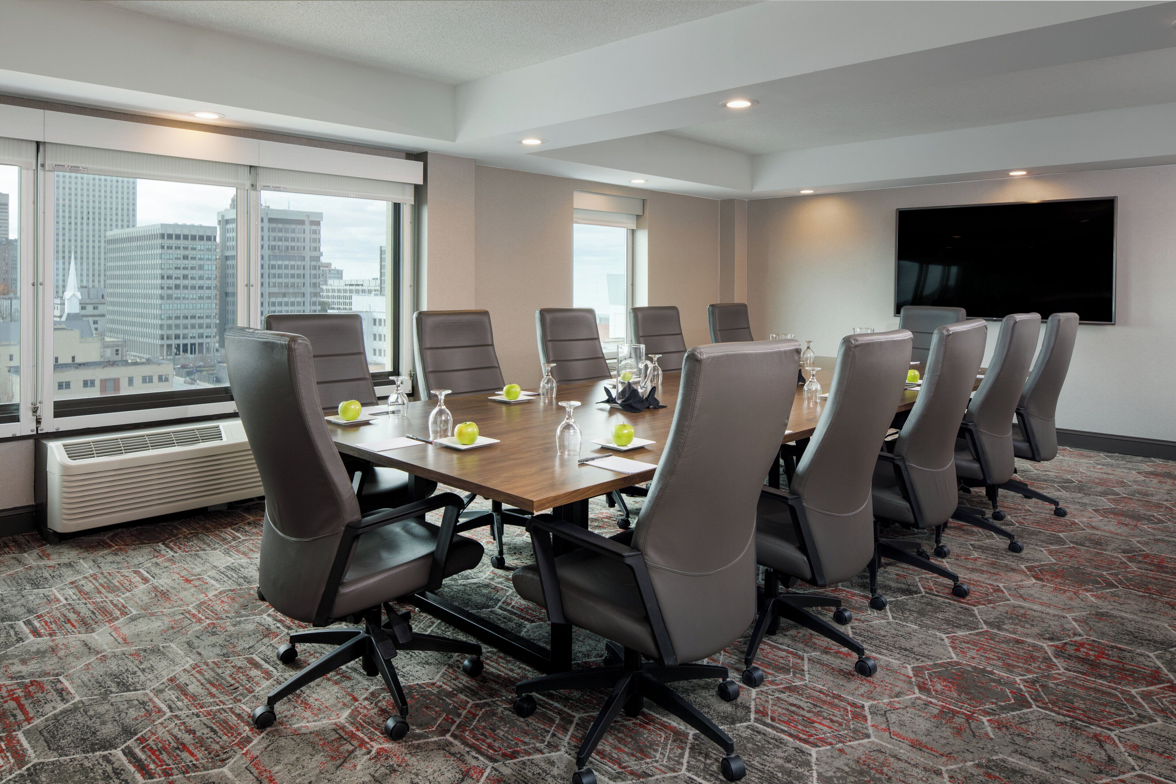 Un salón de conferencias con una mesa larga, varias sillas y un gran ventanal con vistas a la ciudad.