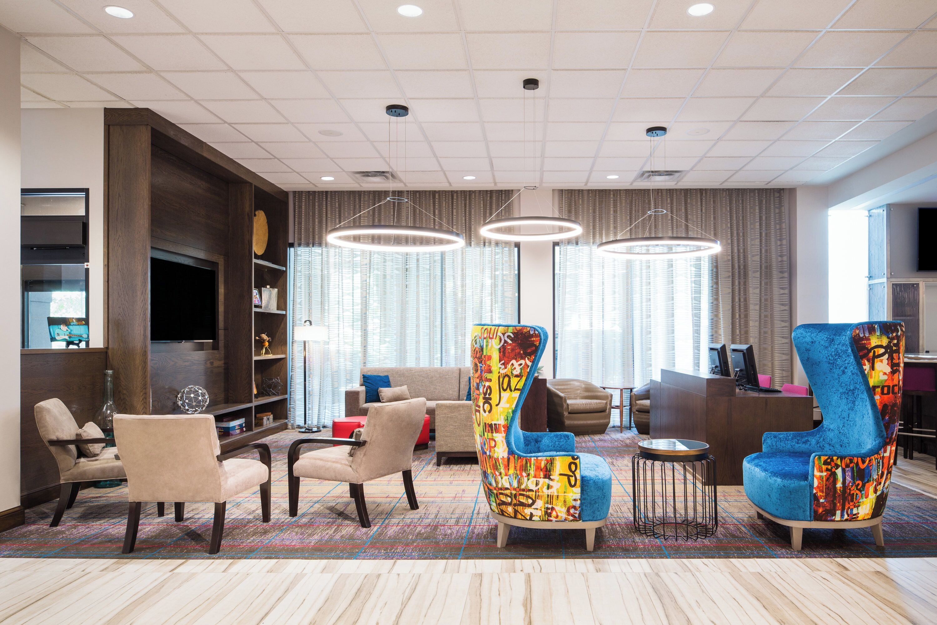 A modern hotel lobby with a seating area, a reception desk, and a television.