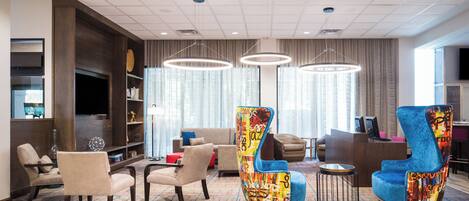 A modern hotel lobby with a seating area, a reception desk, and a television.