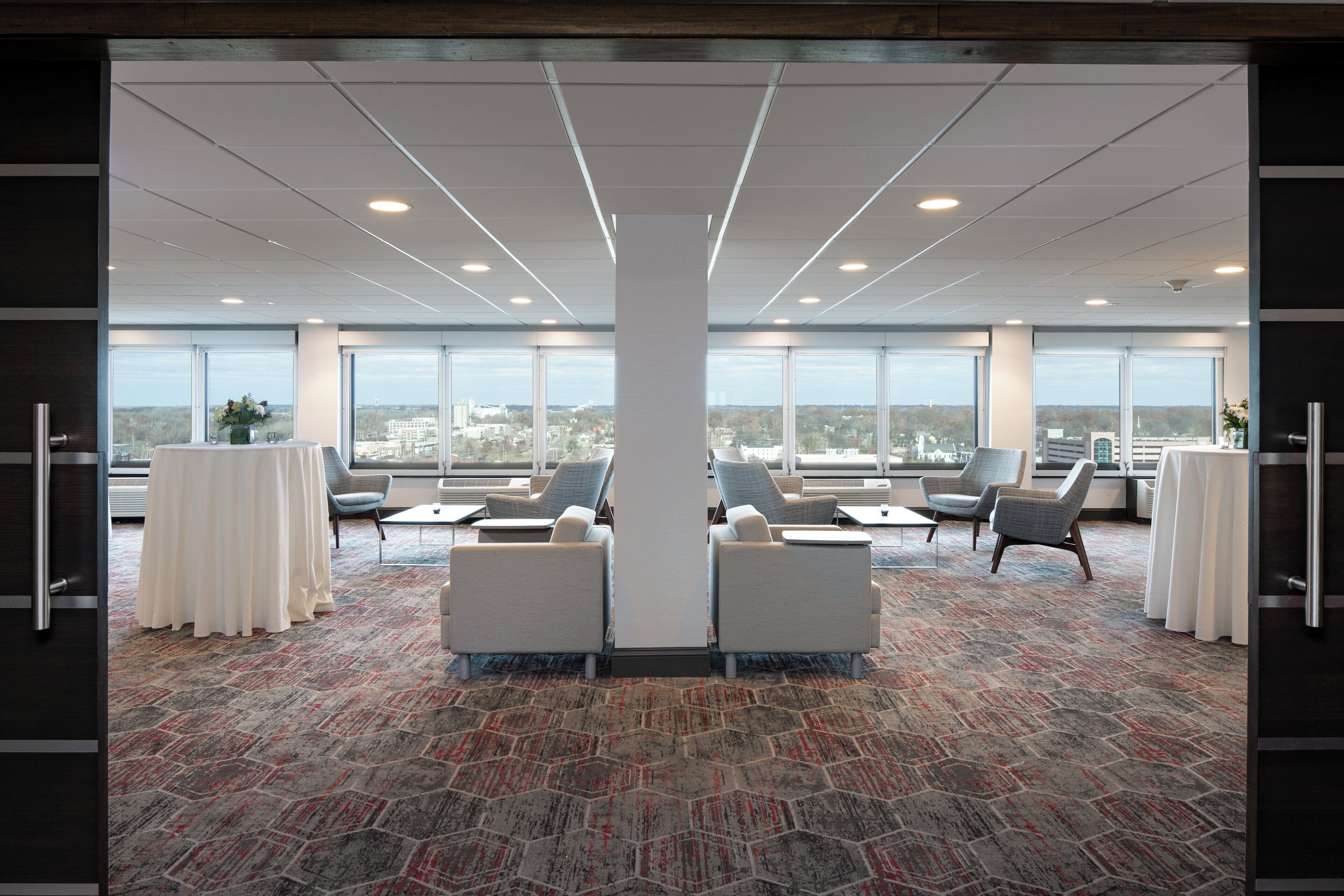 A spacious conference room with large windows, multiple seating areas, and a patterned carpet.