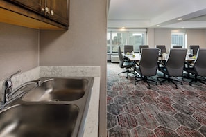 Habitación de hotel con cocina, una mesa de comedor y sillas, y vistas de la ciudad a través de amplias ventanas.