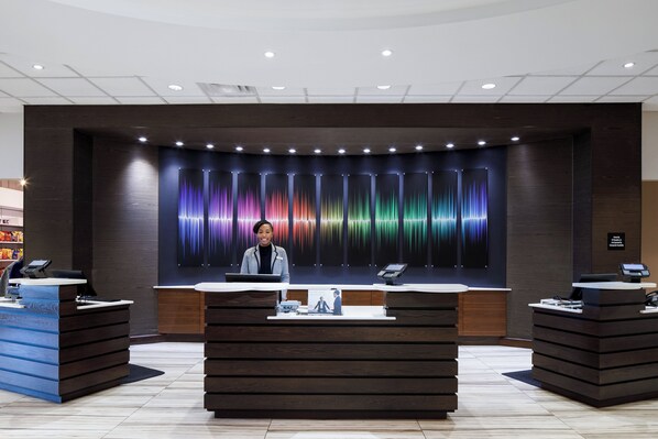 Zona de recepción con diseño moderno, que incluye un mostrador central con una computadora y una pantalla digital, flanqueado por dos mostradores más pequeños.
