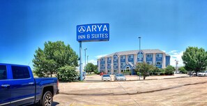 Une enseigne bleue indiquant « ARYA INN & SUITES », avec un immeuble à plusieurs étages en arrière-plan.