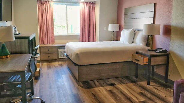 Une chambre d’hôtel avec un lit, des tables de chevet, un bureau, une chaise et une fenêtre avec des rideaux.