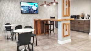 Une cuisine moderne avec un îlot central en bois, des chaises noires et un téléviseur fixé au mur.