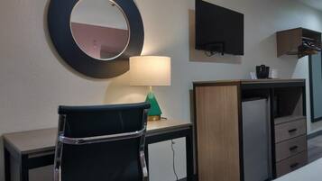A hotel room with a desk, a chair, a TV mounted on the wall, a lamp, and a wardrobe.
