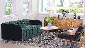 Un canapé vert, une chaise noire, une petite table ronde et un meuble en bois sur lequel est posé un appareil photo sur un trépied.