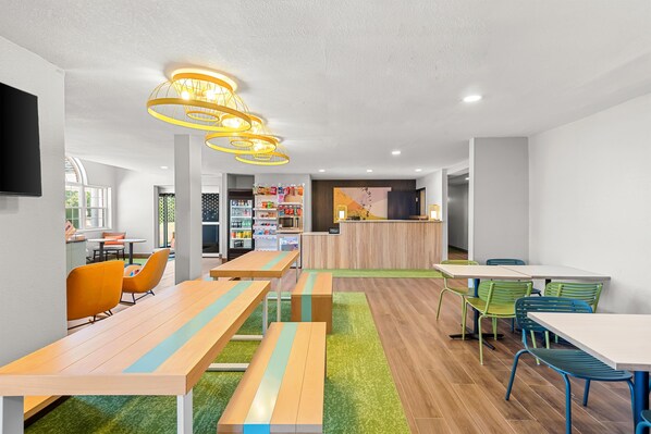 A modern hotel lobby with wooden tables and chairs, a reception desk, and a vending machine.
