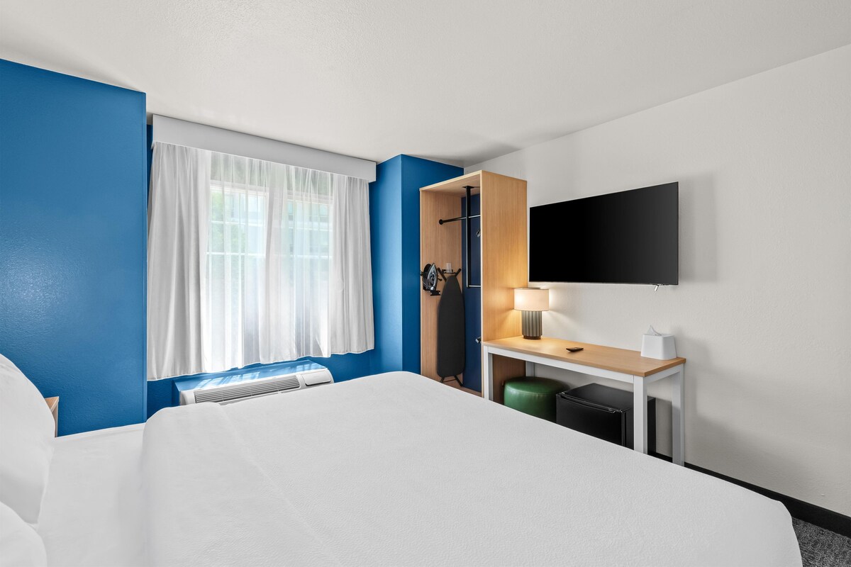 A hotel room with a bed, a desk with a lamp, a television, and a window with curtains.