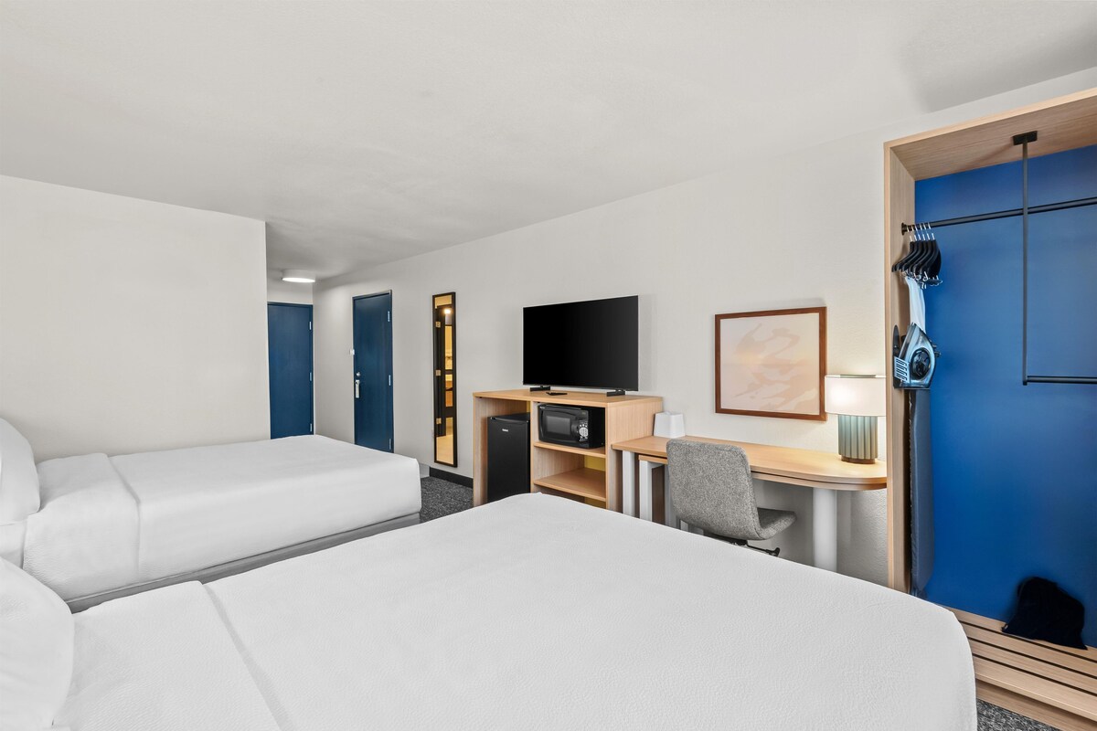 A hotel room with two beds, a desk with a computer, a television, and a wardrobe.