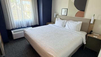Habitación de hotel con una cama grande, una ventana con cortinas, un radiador, una mesita de noche con un teléfono y una obra de arte colgada en la pared.