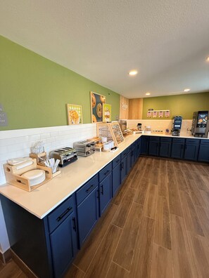 A modern kitchen with a long counter, wooden cabinets, and a coffee machine.