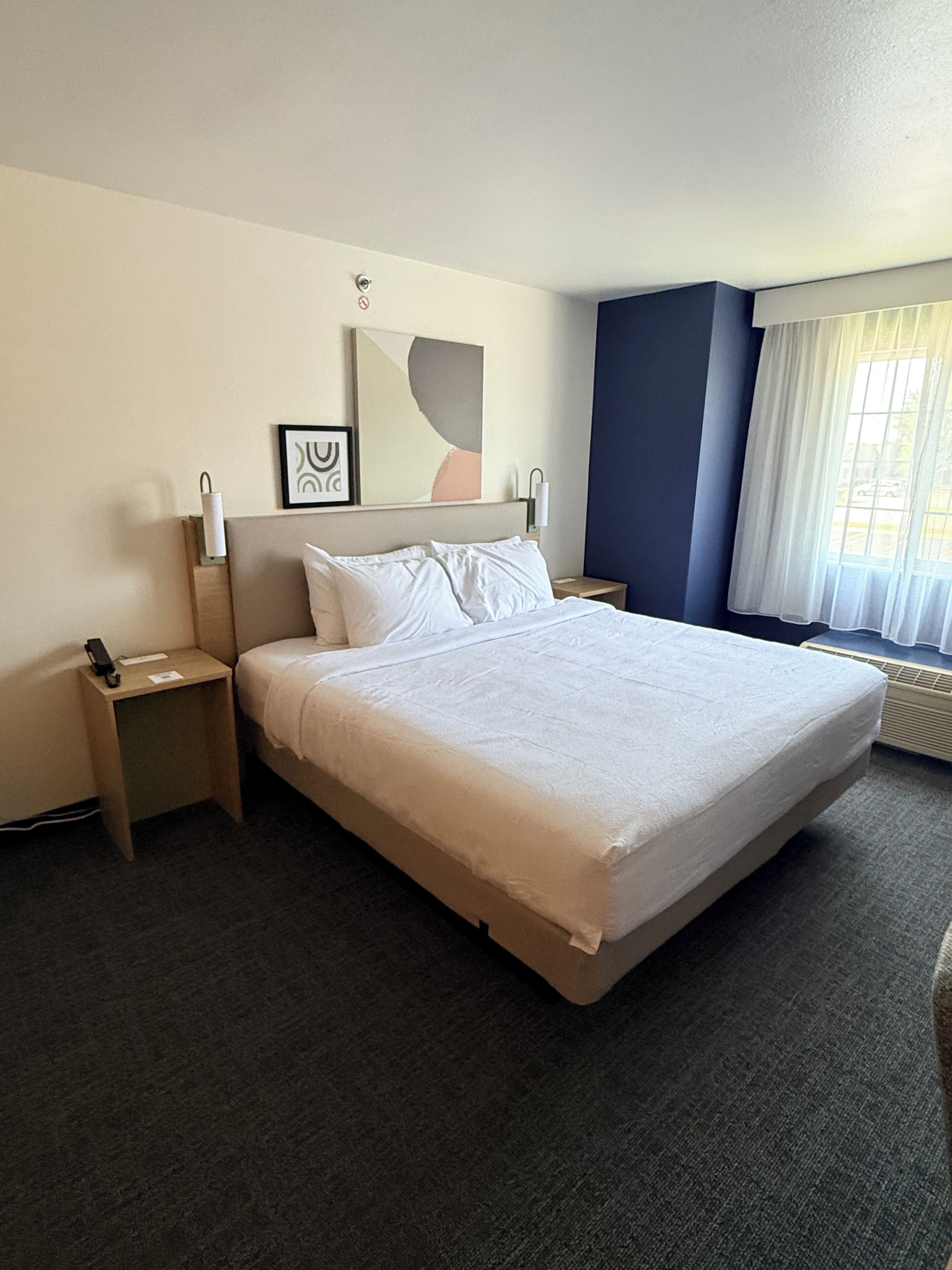 A hotel room with a large bed, bedside tables, a nightstand, a mirror, and a window with curtains.