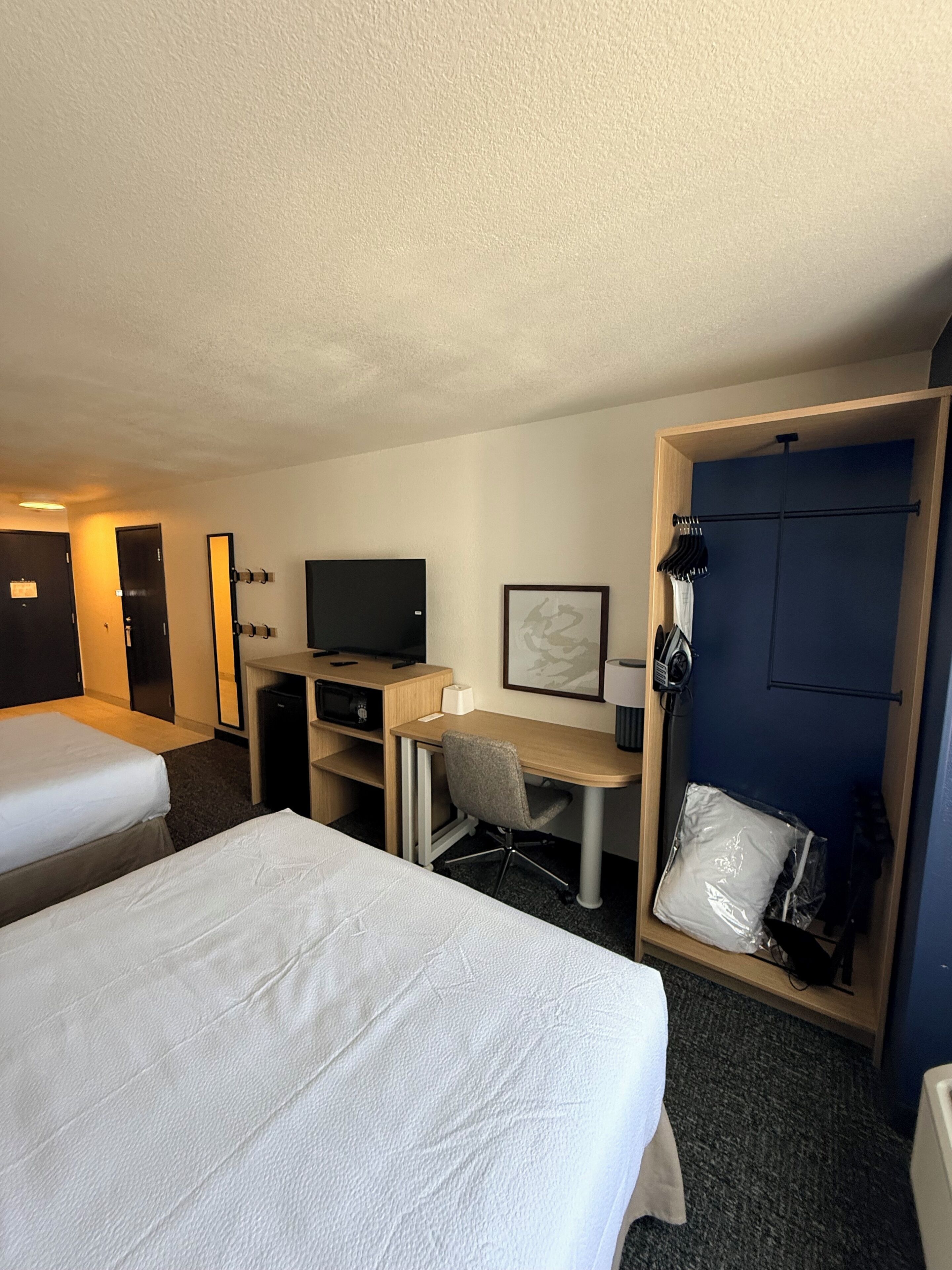 Una habitación de hotel con dos camas, un escritorio con una silla, televisión, armario y puerta.