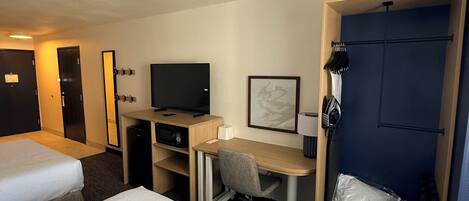Una habitación de hotel con dos camas, un escritorio con una silla, televisión, armario y puerta.