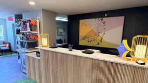 A hotel reception desk with a green artificial turf rug, a wall-mounted artwork, and a shelf with snacks. - Spark by Hilton Appleton (Appleton)