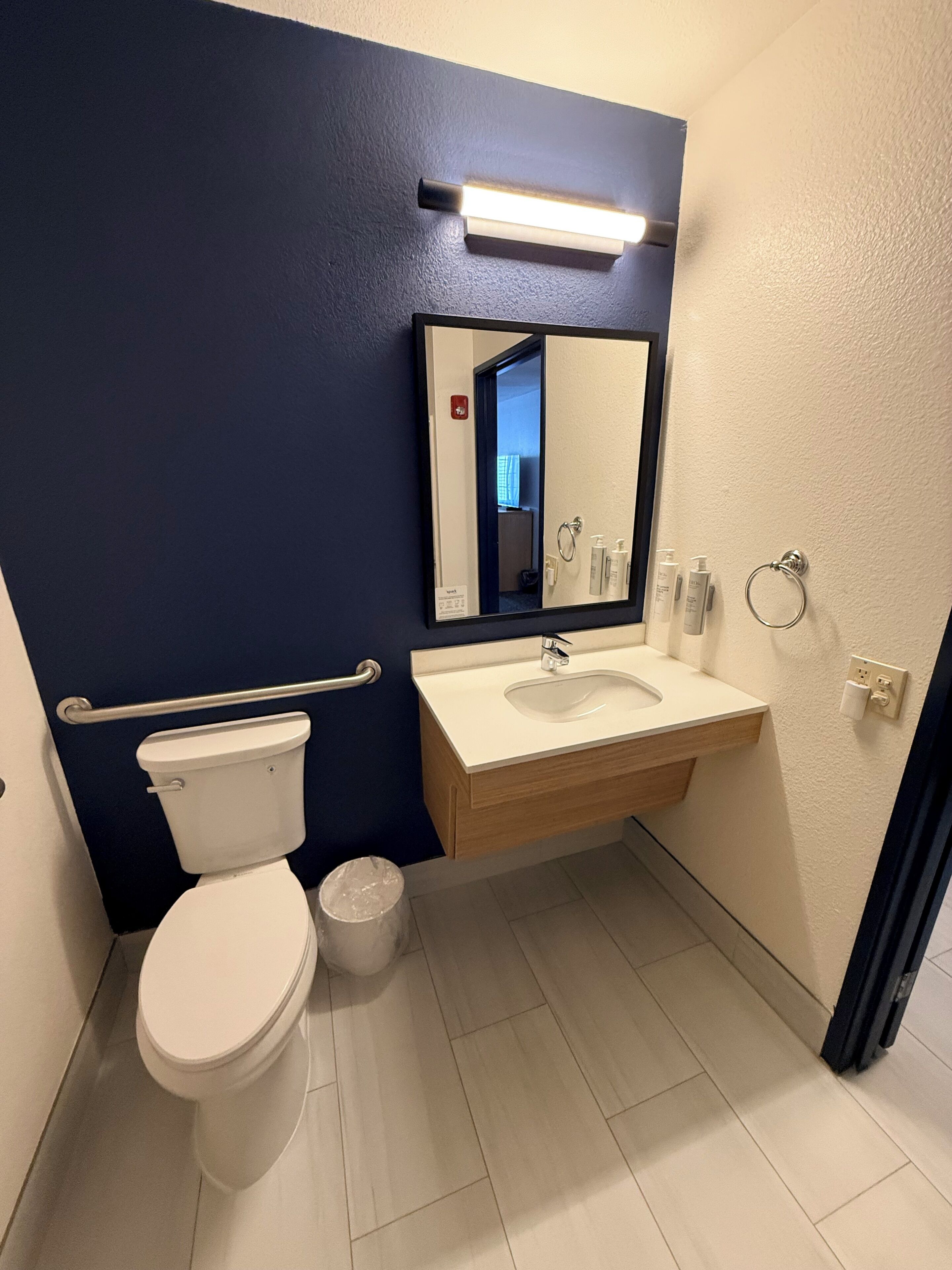 A bathroom with a white toilet, a sink with a mirror above it, and a blue wall.