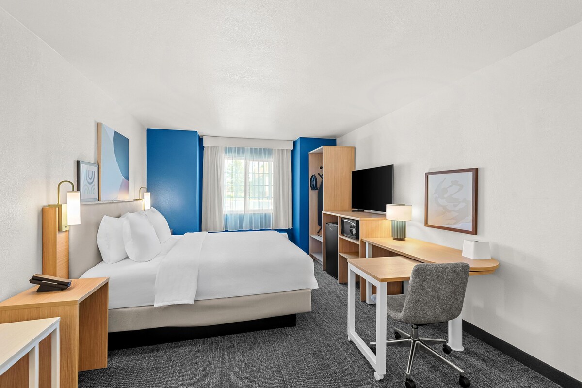 A hotel room with a bed, desk, chair, television, and a window with curtains.