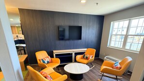 A modern living room with a flat-screen TV, orange rocking chairs, a round coffee table, and a large window. - Spark by Hilton Appleton (Appleton)