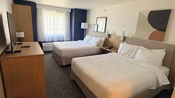 Habitación de hotel con dos camas, un escritorio, una silla, un televisor, una lámpara y un cuadro en la pared.