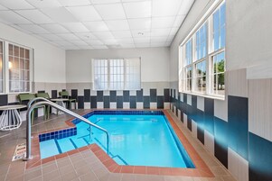 Una piscina interior con suelo de baldosas, una escalera metálica y una ventana con vistas al exterior.