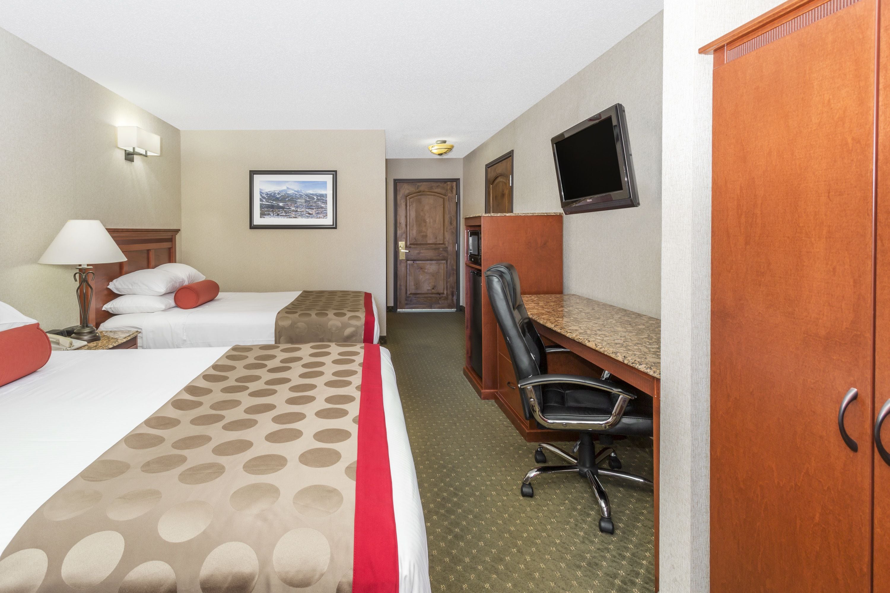 Une chambre d’hôtel avec deux lits, un bureau, une chaise, une télévision et une porte.
