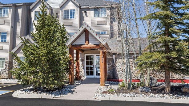 A multi-story building with a stone facade, a wooden entrance canopy, and a snow-covered ground. - Ramada by Wyndham Frisco (Frisco)