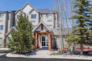 A multi-story building with a stone facade, a wooden entrance canopy, and a snow-covered ground. - Ramada by Wyndham Frisco (Frisco)