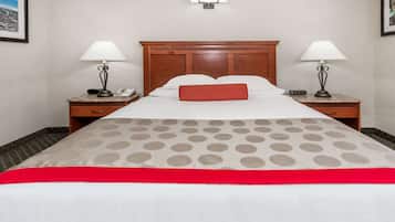 A hotel room with a wooden headboard, two bedside tables with lamps, a bed with a red pillow, and a view of the city through the window.