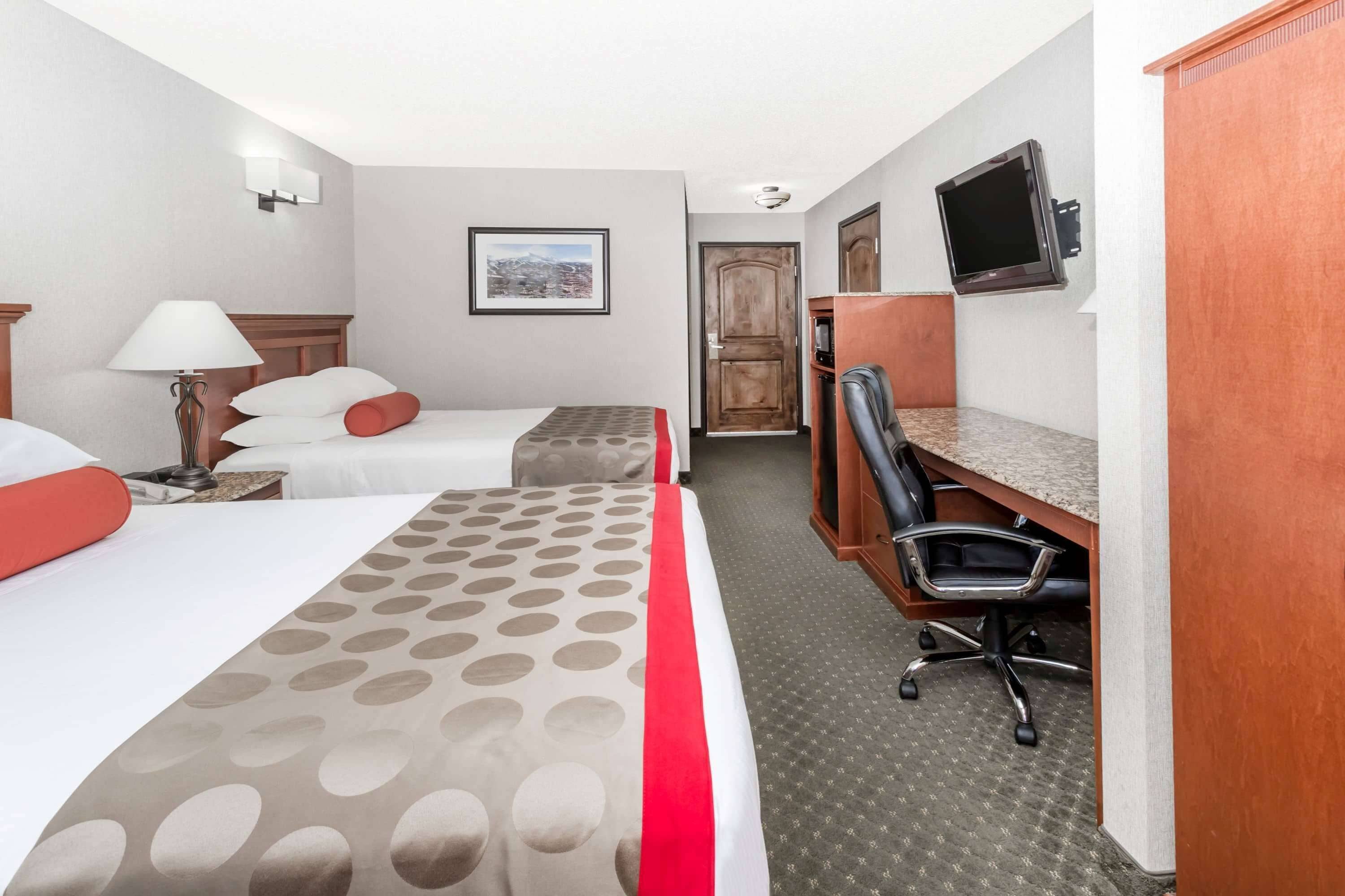 Habitación de hotel con dos camas, un escritorio, una silla, un televisor y un cuadro en la pared.