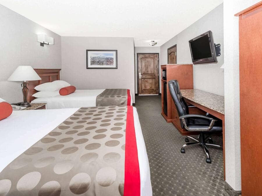 Een hotelkamer met twee bedden, een bureau, een stoel, een televisie en een lijst met een afbeelding aan de muur.