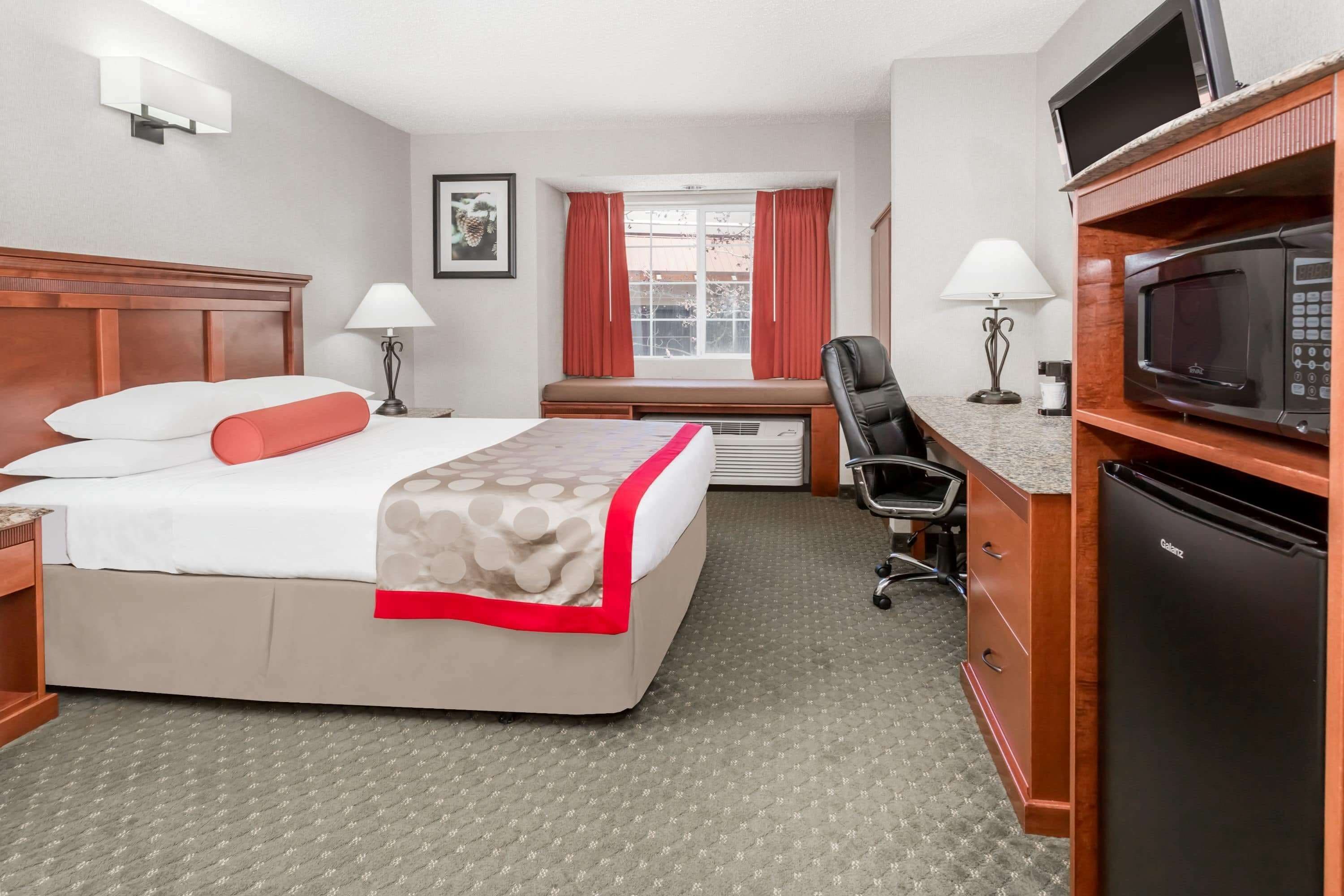 A hotel room with a bed, desk, chair, microwave, and refrigerator.