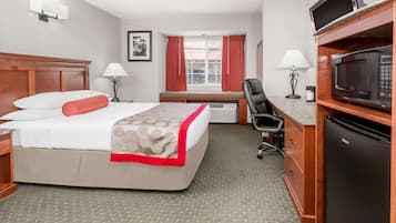 A hotel room with a bed, desk, chair, microwave, and refrigerator.
