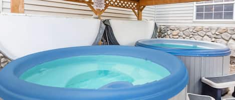 Two hot tubs with wooden benches under a wooden pergola.