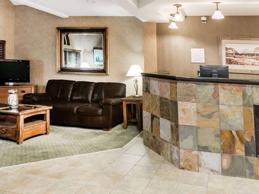 A hotel lobby with a leather sofa, a wooden coffee table, a TV, a reception desk, and a stone wall with a framed picture.