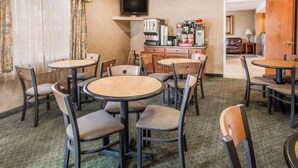 A hotel room with a dining area featuring round tables and chairs, a coffee machine, and a television on a shelf. - Ramada by Wyndham Frisco (Frisco)